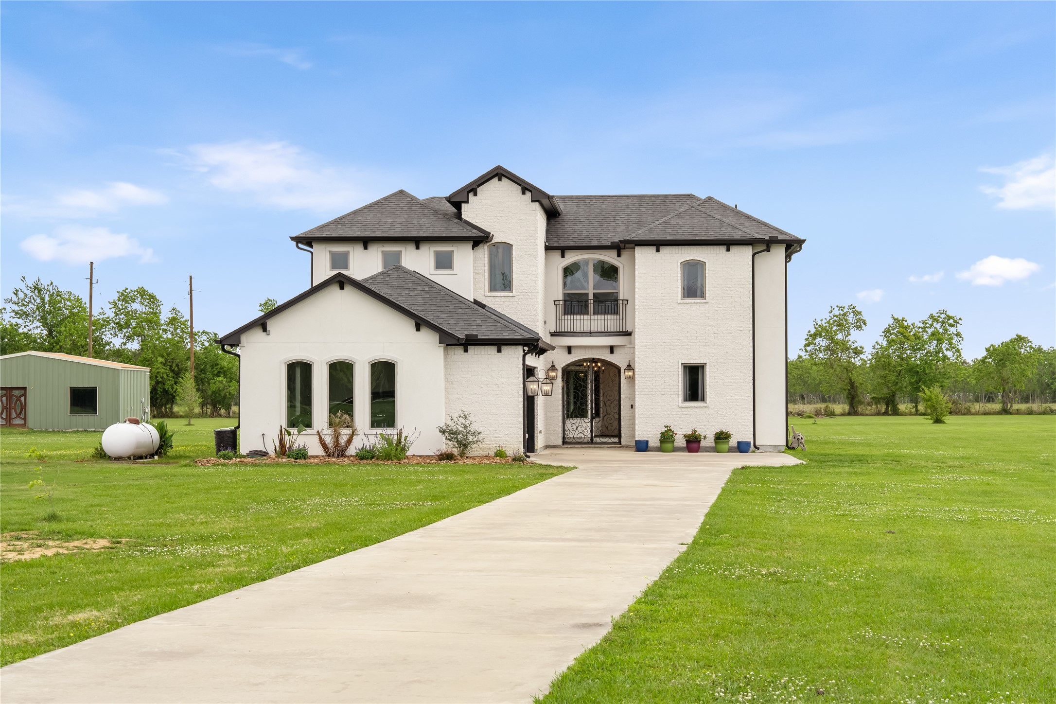 2856 Wolcek Road Crosby, TX 77532 - Photo 2 of 48 Charming two-story white brick home with a dark roof, featuring an elegant front entrance and large windows. It's set on a spacious lot with a long driveway leading up to the house.