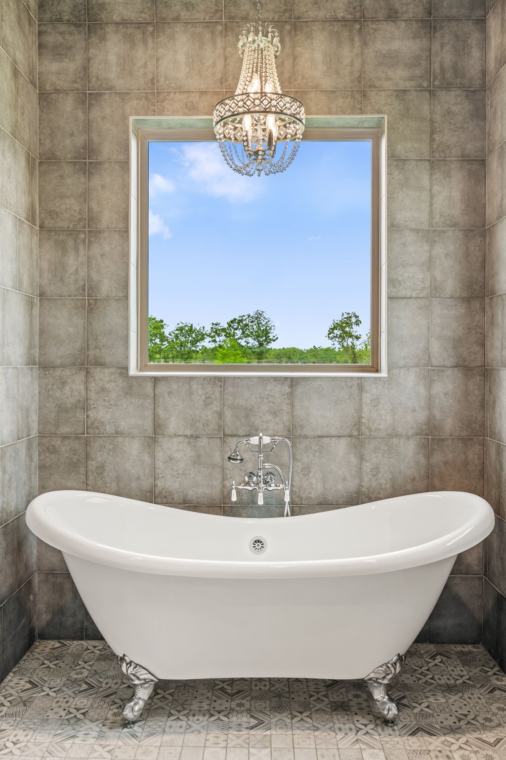 2856 Wolcek Road Crosby, TX 77532 - Photo 21 of 48 This bathroom features a luxurious clawfoot bathtub under an elegant chandelier, with a large window offering serene views, all set against stylish tiled walls and floors.