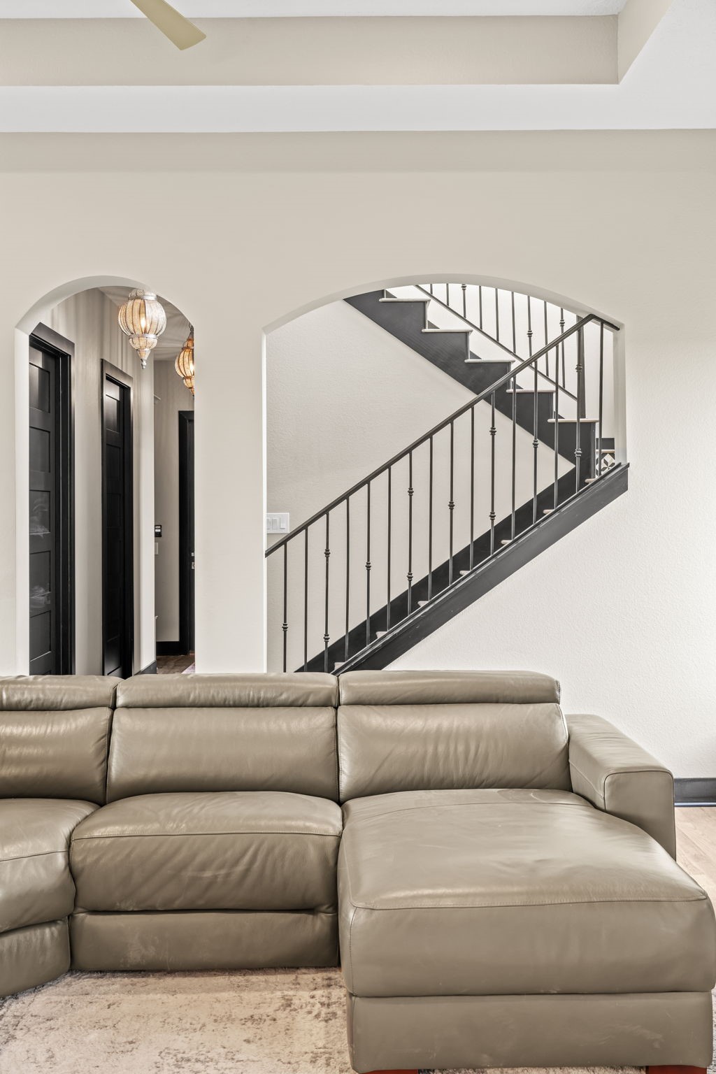 2856 Wolcek Road Crosby, TX 77532 - Photo 28 of 48 This photo showcases a modern living area with a sleek sectional sofa, arched entryways, and a stylish staircase with metal railings, creating an open and inviting space.