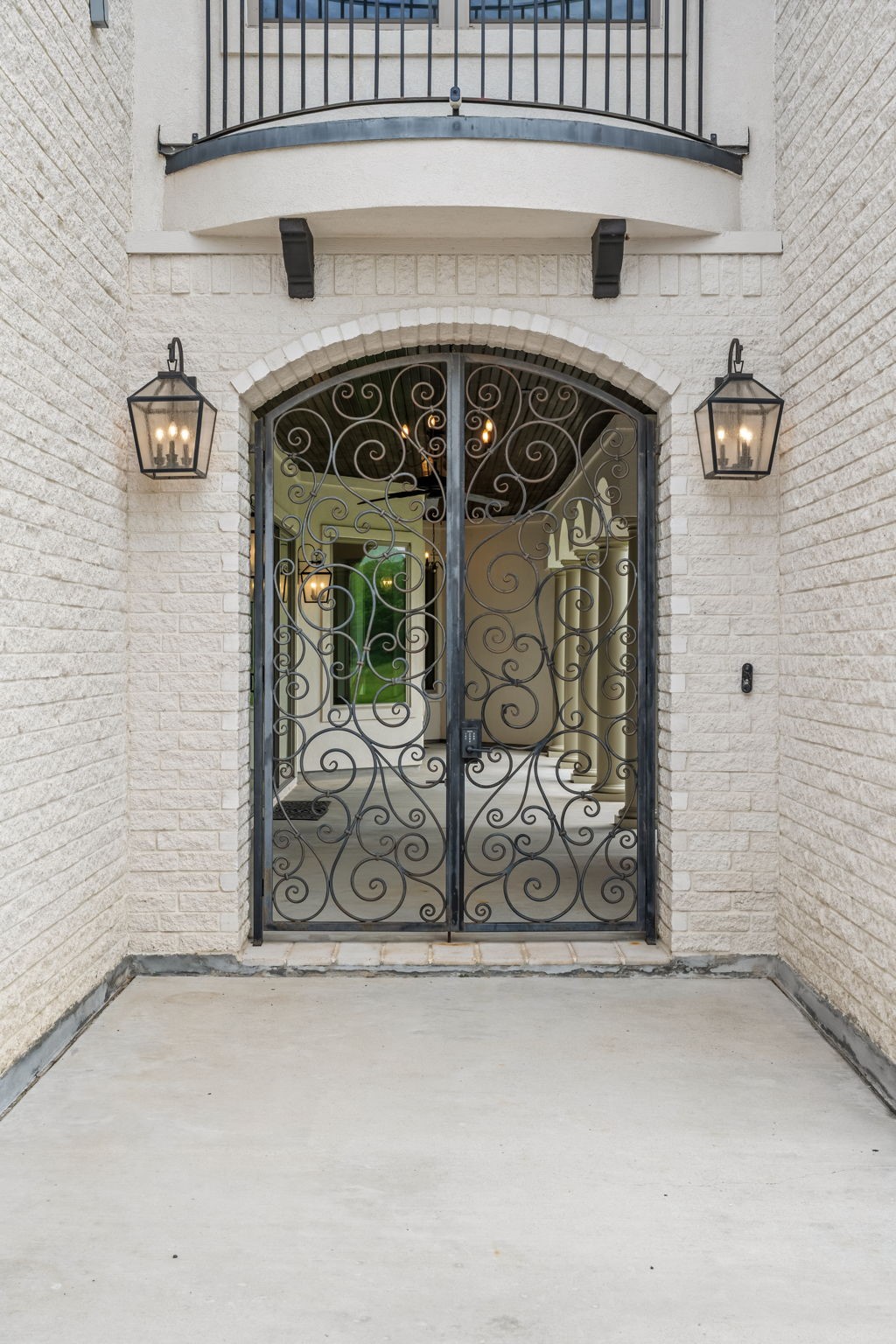 2856 Wolcek Road Crosby, TX 77532 - Photo 3 of 48 This photo showcases an elegant front entrance with decorative wrought iron doors, set between light brick walls. Flanked by stylish lantern-style lights, it offers a grand and inviting entryway to the home.