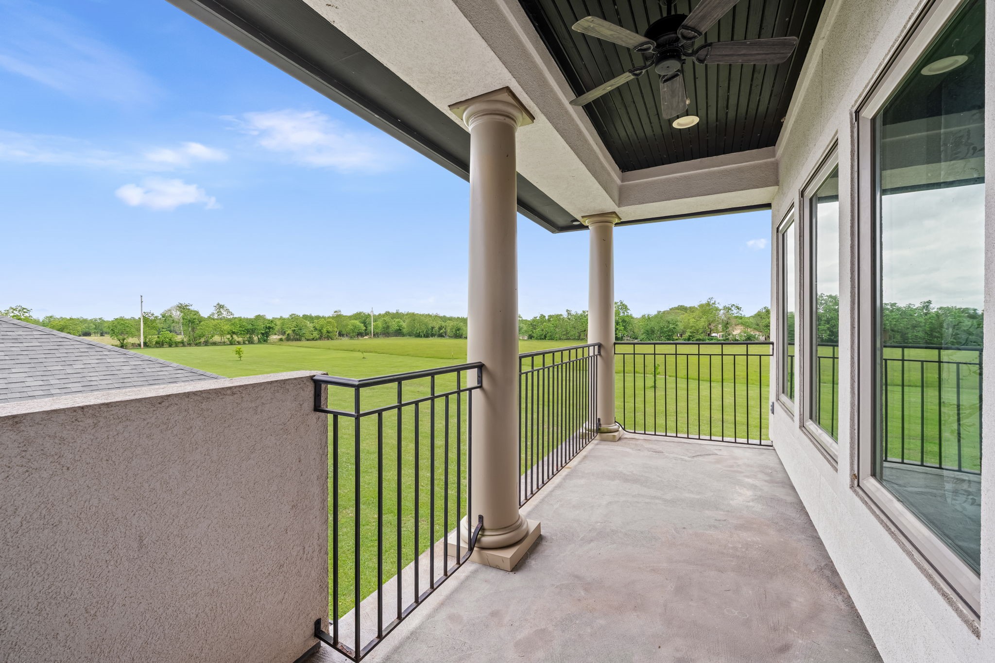 2856 Wolcek Road Crosby, TX 77532 - Photo 35 of 48 Spacious balcony with elegant columns and a ceiling fan, offering expansive views of a lush green landscape. The space is ideal for relaxing or entertaining while enjoying the serene natural surroundings.