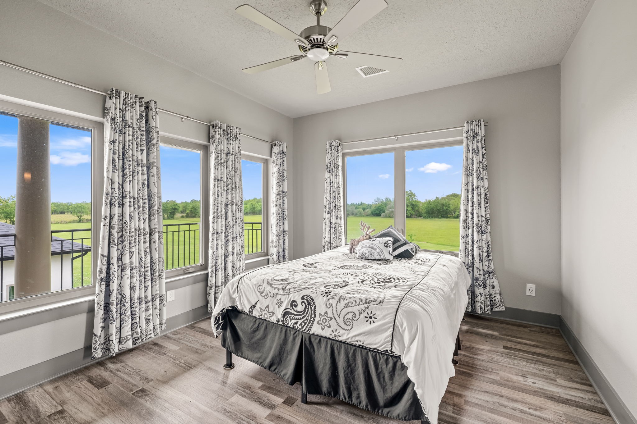 2856 Wolcek Road Crosby, TX 77532 - Photo 36 of 48 This bright ensuite bedroom features large windows with scenic views of greenery, stylish patterned curtains, and a modern ceiling fan. The space is accented by engineered wood flooring and a gorgeous private bathroom.