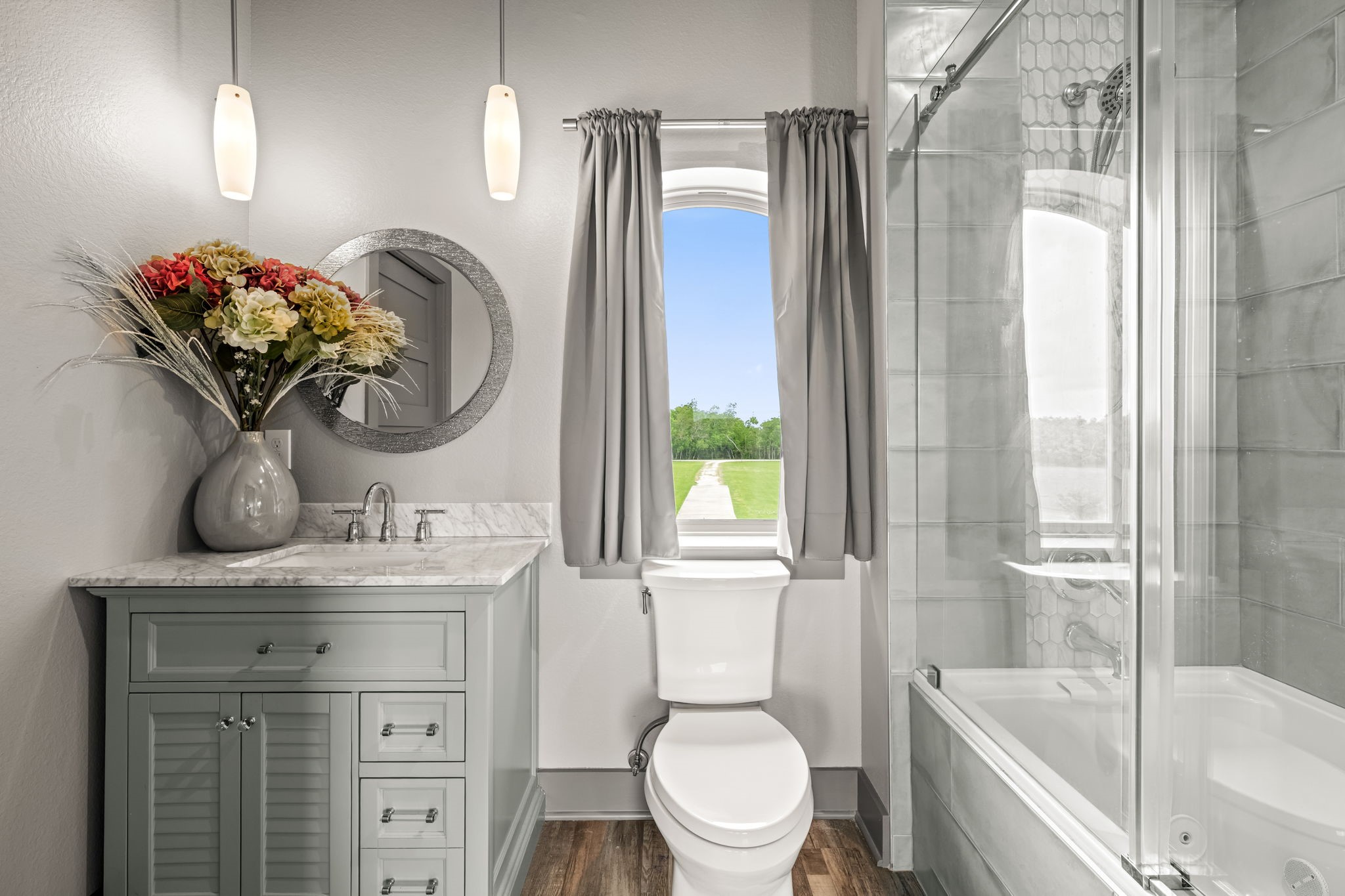 2856 Wolcek Road Crosby, TX 77532 - Photo 38 of 48 This bathroom features a modern design with a stylish vanity, marble countertop, and round mirror. It includes a glass-enclosed shower, natural lighting from a window, and elegant fixtures, creating a fresh and inviting space.