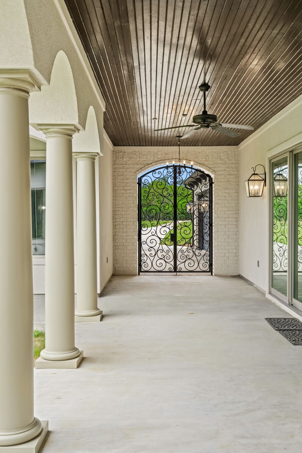 2856 Wolcek Road Crosby, TX 77532 - Photo 5 of 48 a spacious, covered porch with elegant columns, a wooden ceiling, a ceiling fan, and decorative wrought iron gates, offering a sophisticated and welcoming entrance.