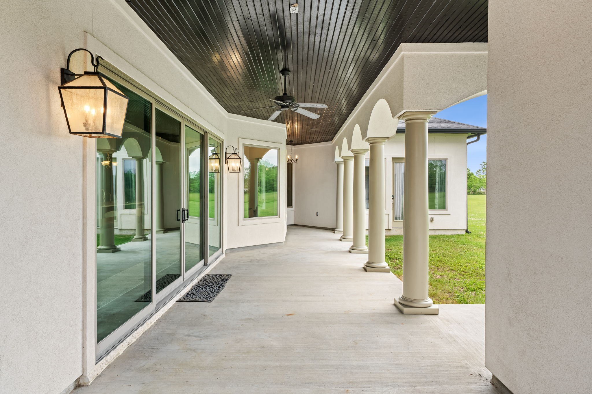 2856 Wolcek Road Crosby, TX 77532 - Photo 6 of 48 This photo showcases a spacious covered patio with elegant columns, a dark wood ceiling, and stylish lantern lighting. Large sliding glass doors open to a lush, grassy yard, creating a seamless indoor-outdoor living space. There is an electrical rough-in for a pool addition located in this area.