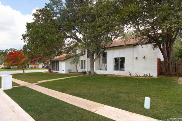 a view of a white house in front of a big yard with large trees