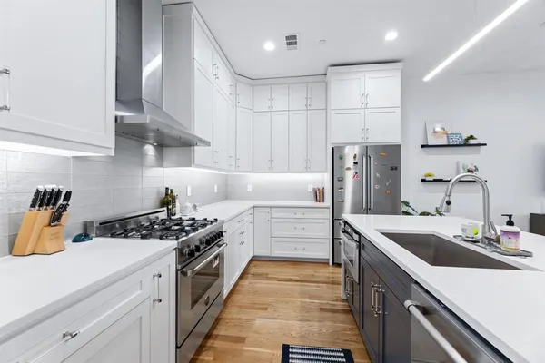 a large kitchen with stainless steel appliances a stove a sink dishwasher and a dining table with wooden floor