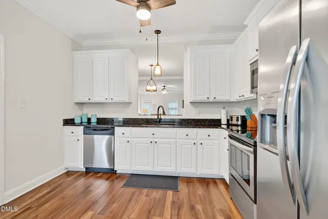 a kitchen with stainless steel appliances granite countertop a refrigerator a sink dishwasher a stove and white cabinets with wooden floor