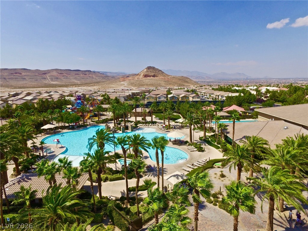 87 Tall Ruff Drive Las Vegas, NV 89148 - Photo 1 of 71 An aerial panorama reveals a vast community pool surrounded by palm trees, set against distant mountains.