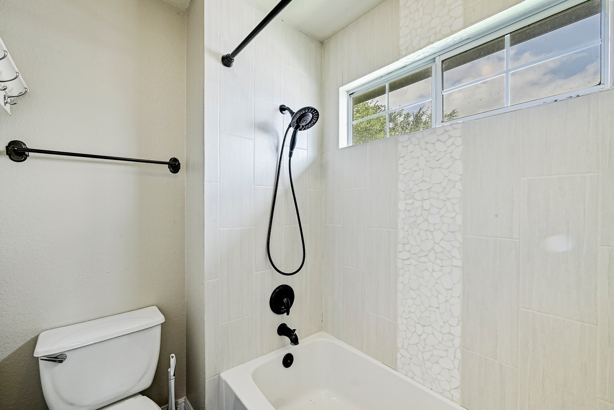 2408 Amen Corner Road Pflugerville, TX 78660 - Photo 31 of 40 Bathtub with matte black fixtures, subway tile surround, pebble tile accent, and transom window
