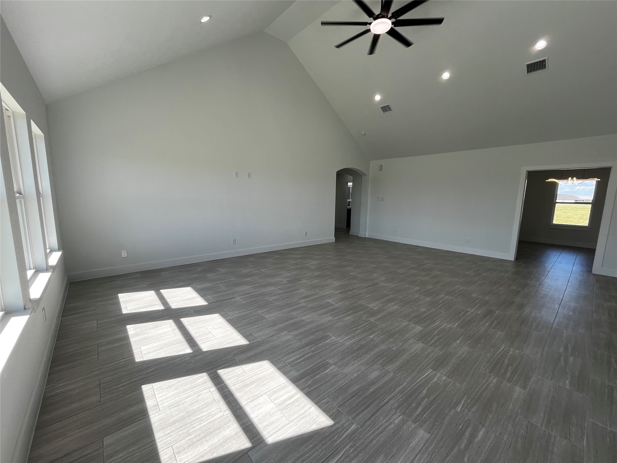471 Buffalo Trail Angleton, TX 77515 - Photo 6 of 35 Spacious living area with high vaulted ceilings and large windows allowing ample natural light. Sleek tile flooring and modern ceiling fan enhance the contemporary feel. Adjacent room visible through an archway, offering potential for versatile use.