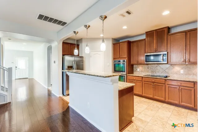 a kitchen with kitchen island granite countertop wooden cabinets a stove a sink and a oven