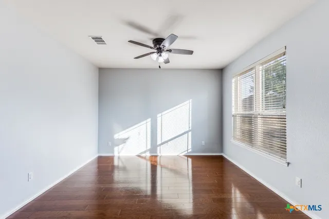 an empty room with wooden floor fan and windows