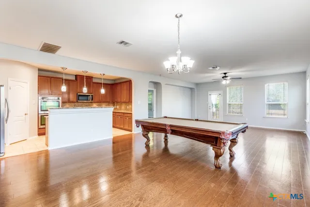 a room with wooden floors pool table and chairs