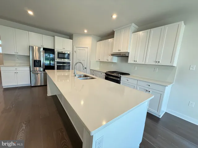 a large kitchen with stainless steel appliances a large counter top a stove a refrigerator a sink a center island and cabinets