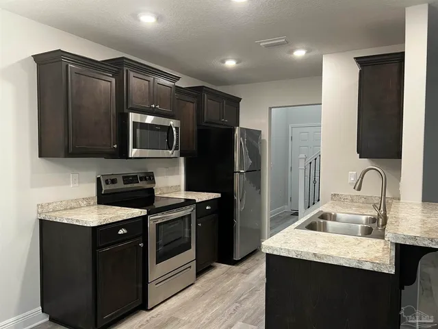 a kitchen with stainless steel appliances granite countertop a stove a sink and a refrigerator with wooden floor