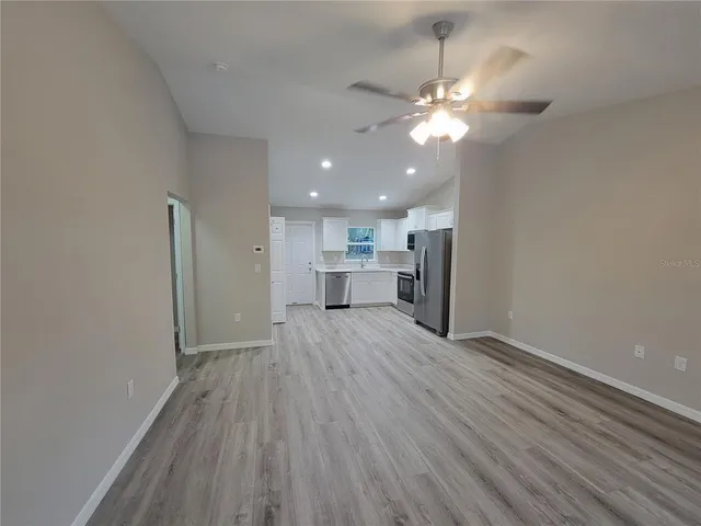 a view of a room with wooden floor a ceiling fan and kitchen