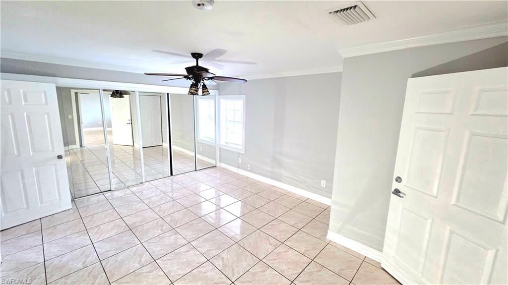 5529 Hardee Street Naples, FL 34113 - Photo 8 of 17 Spacious room featuring light-colored tile flooring, full-wall mirrored closet doors, a ceiling fan with integrated lighting, and two windows providing natural light