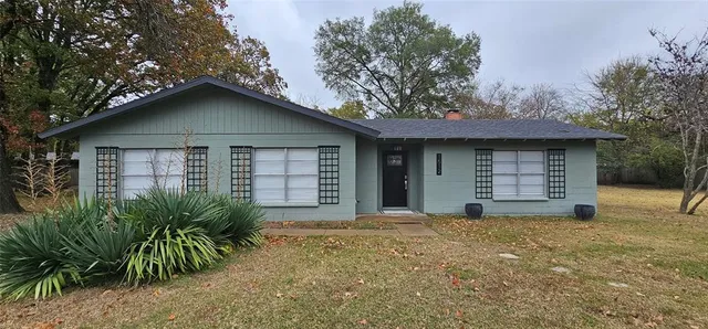 a view of a house with a yard plants and large tree