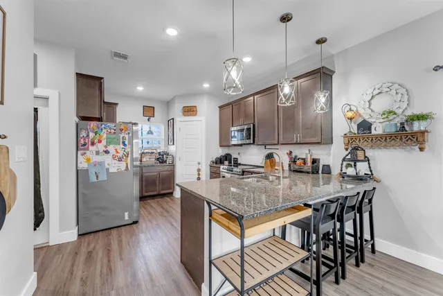 a kitchen with stainless steel appliances granite countertop a stove refrigerator a sink dishwasher a dining table and chairs with wooden floor