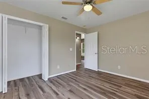 a view of an empty room with wooden floor and a ceiling fan