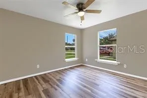 an empty room with wooden floor chandelier fan and windows