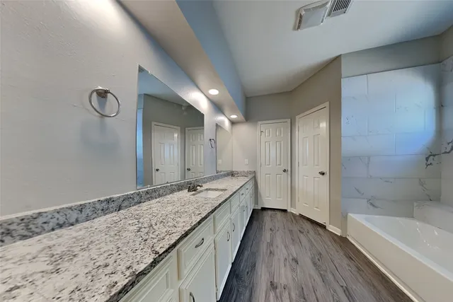 a spacious bathroom with a granite countertop sink a mirror and bathtub