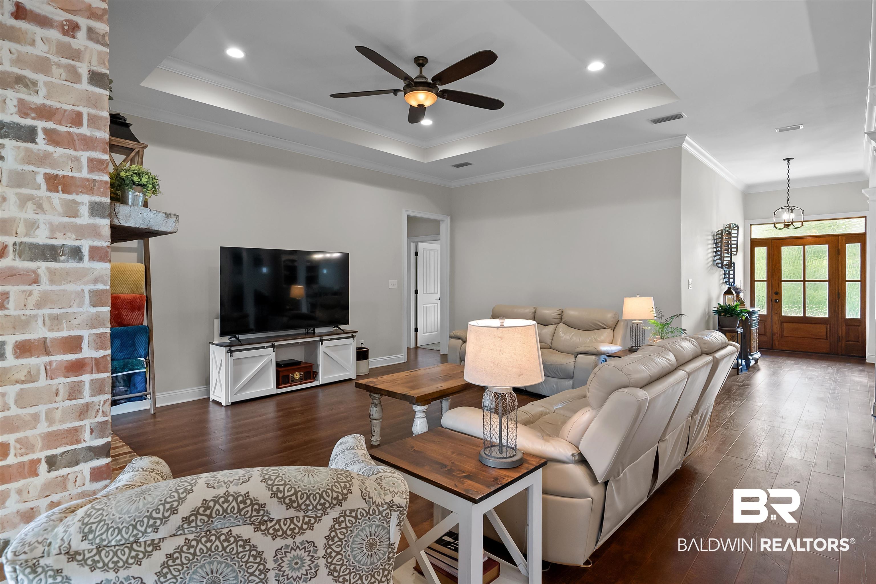 12070 Comalander Road Fairhope, AL 36532 - Photo 7 of 50 Open-concept living area featuring rich wood-finish flooring, a tray ceiling with recessed lighting and a ceiling fan, and a brick-finish accent wall