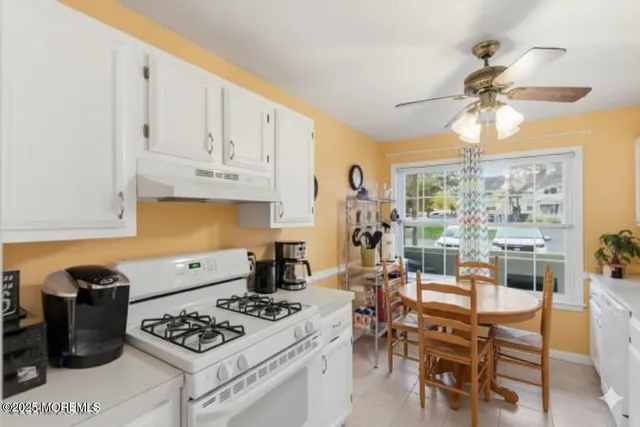 a kitchen with stainless steel appliances granite countertop a stove a sink dishwasher and white cabinets with wooden floor