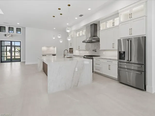 a large white kitchen with stainless steel appliances a large counter top a stove and a refrigerator