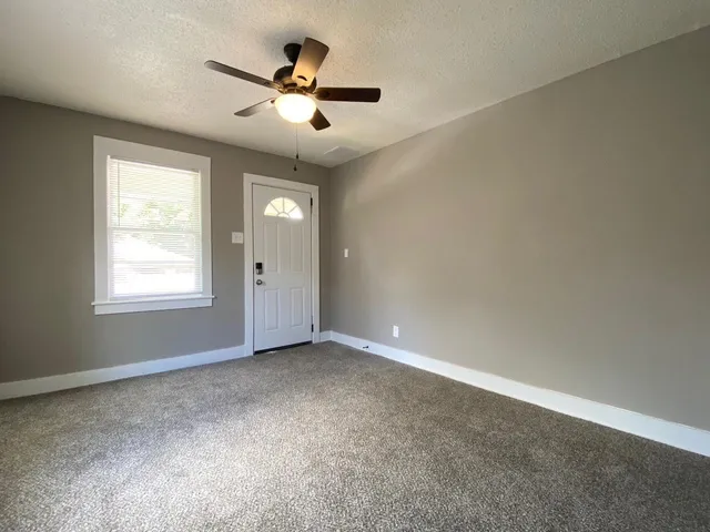 an empty room with chandelier fan and windows