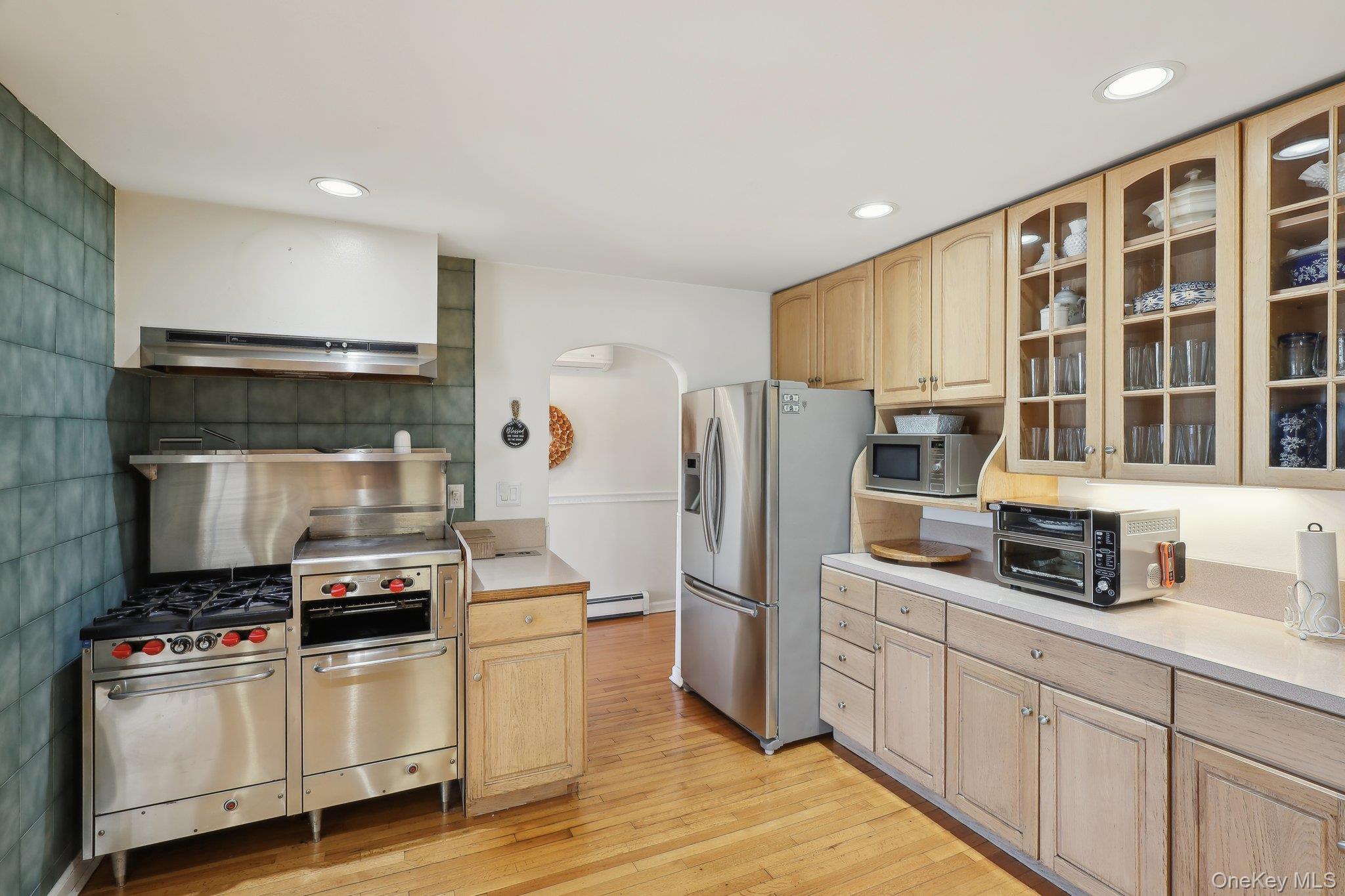230 West Islip Road West Islip, NY 11795 - Photo 16 of 50 Kitchen featuring arched walkways, light wood-type flooring, appliances with stainless steel finishes, baseboard heating, and under cabinet range hood