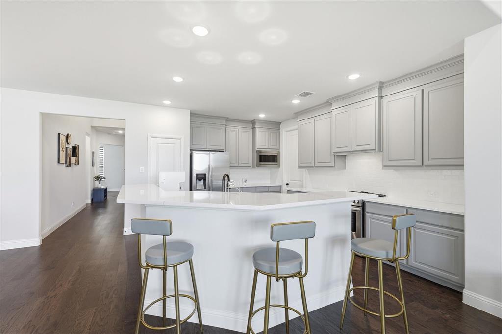 1988 Nottingham Place Allen, TX 75013 - Photo 10 of 40 Kitchen with a breakfast bar area, gray cabinets, appliances with stainless steel finishes, backsplash, and dark wood finished floors