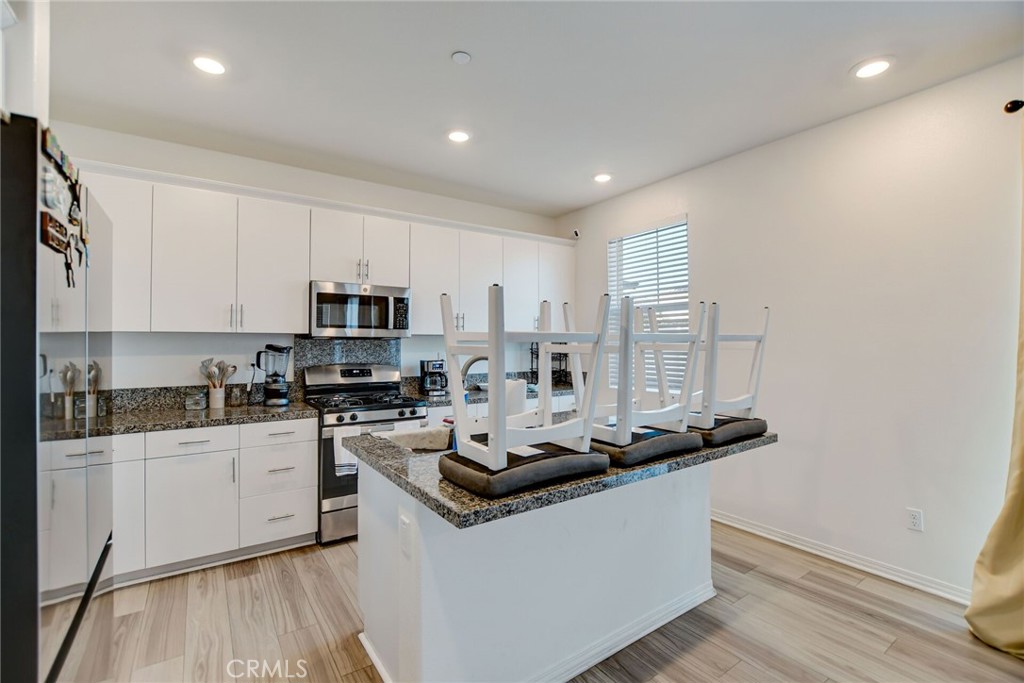 2526 Gunner Ridge Way Rialto, CA 92377 - Photo 14 of 33 a kitchen with stainless steel appliances granite countertop a stove top oven a sink a refrigerator and white cabinets with wooden floor