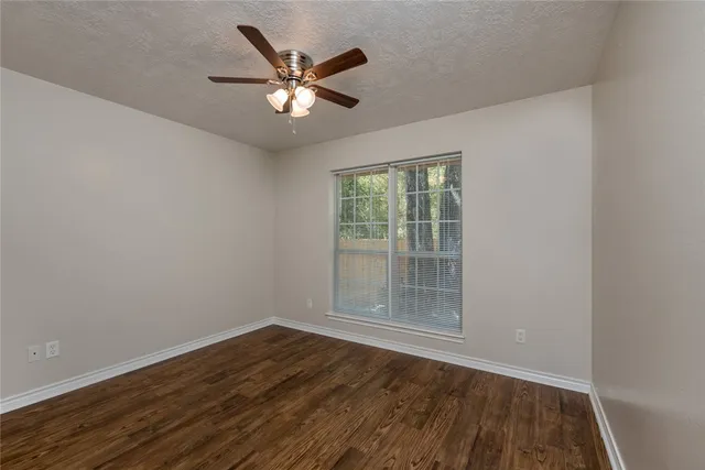 an empty room with wooden floor chandelier fan and windows