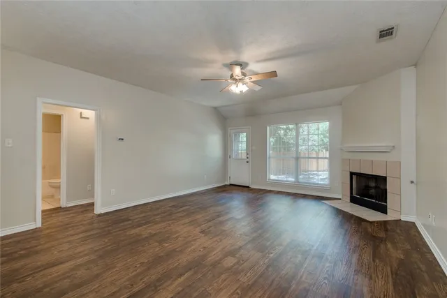 a view of an empty room with wooden floor fireplace and a window