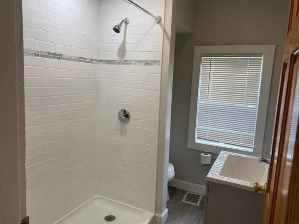 a bathroom with a sink a toilet a shower and a window