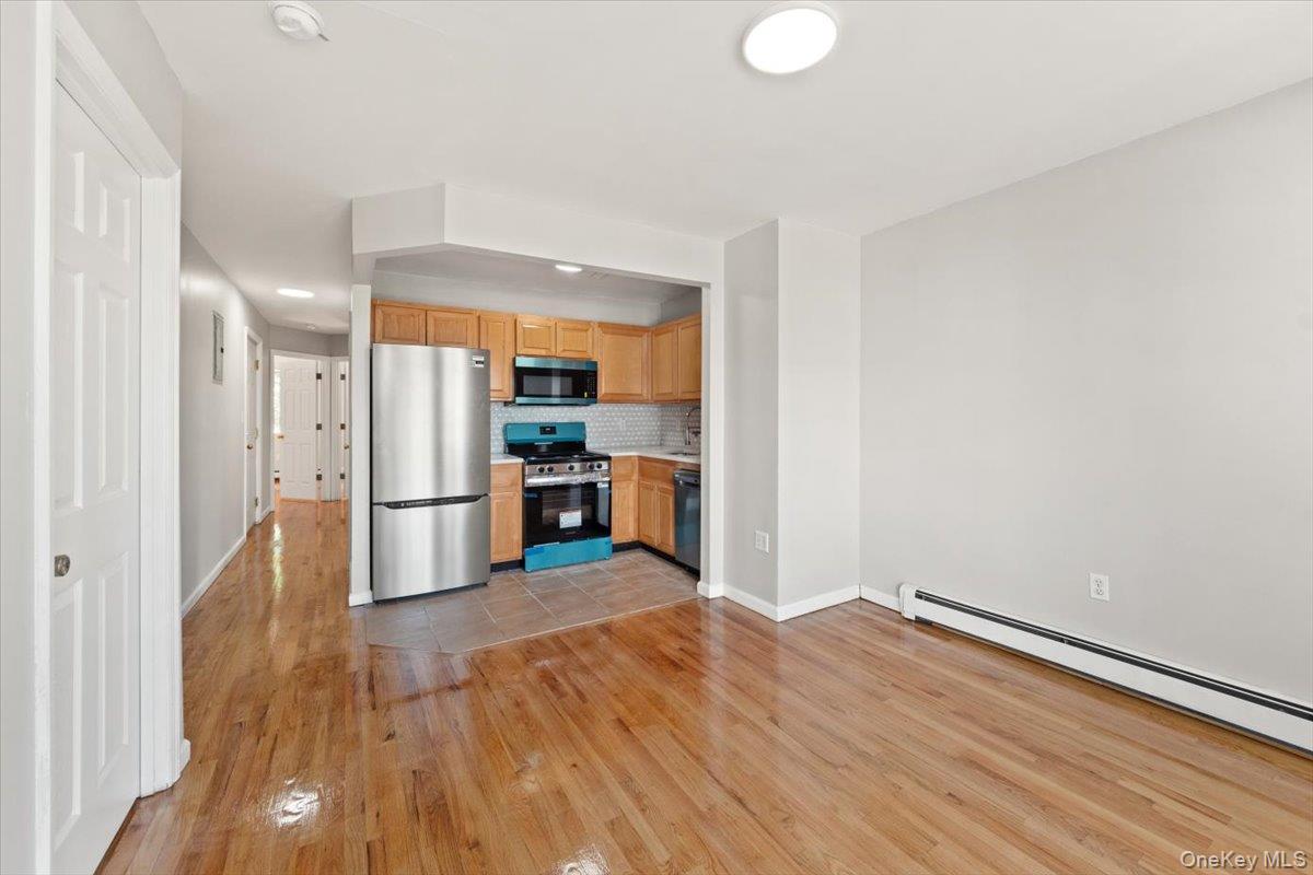 1309 Vreeland Avenue, Unit 3 Bronx, NY 10461 - Photo 3 of 13 Kitchen with appliances with stainless steel finishes, light wood finished floors, a baseboard heating unit, tasteful backsplash, and light countertops