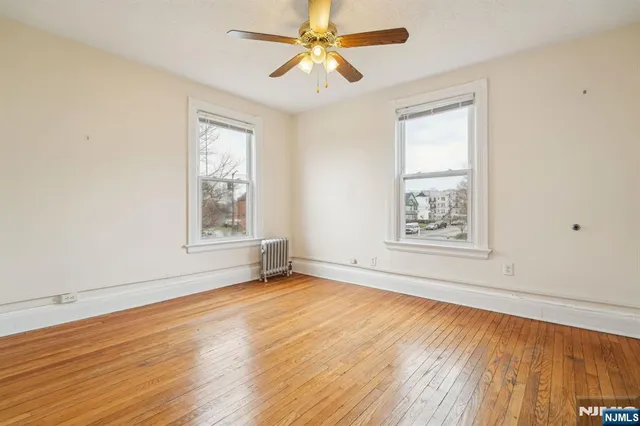 an empty room with wooden floor chandelier fan and windows