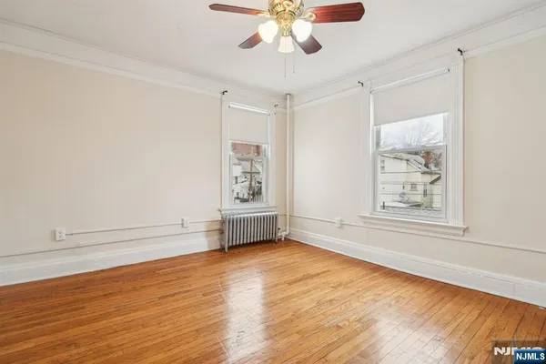 an empty room with wooden floor chandelier fan and windows