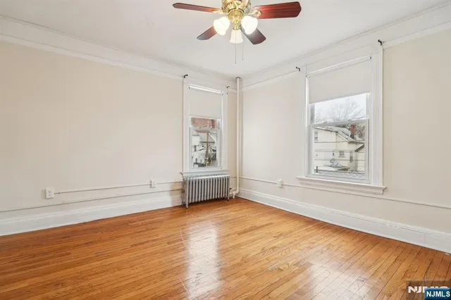 an empty room with wooden floor chandelier fan and windows
