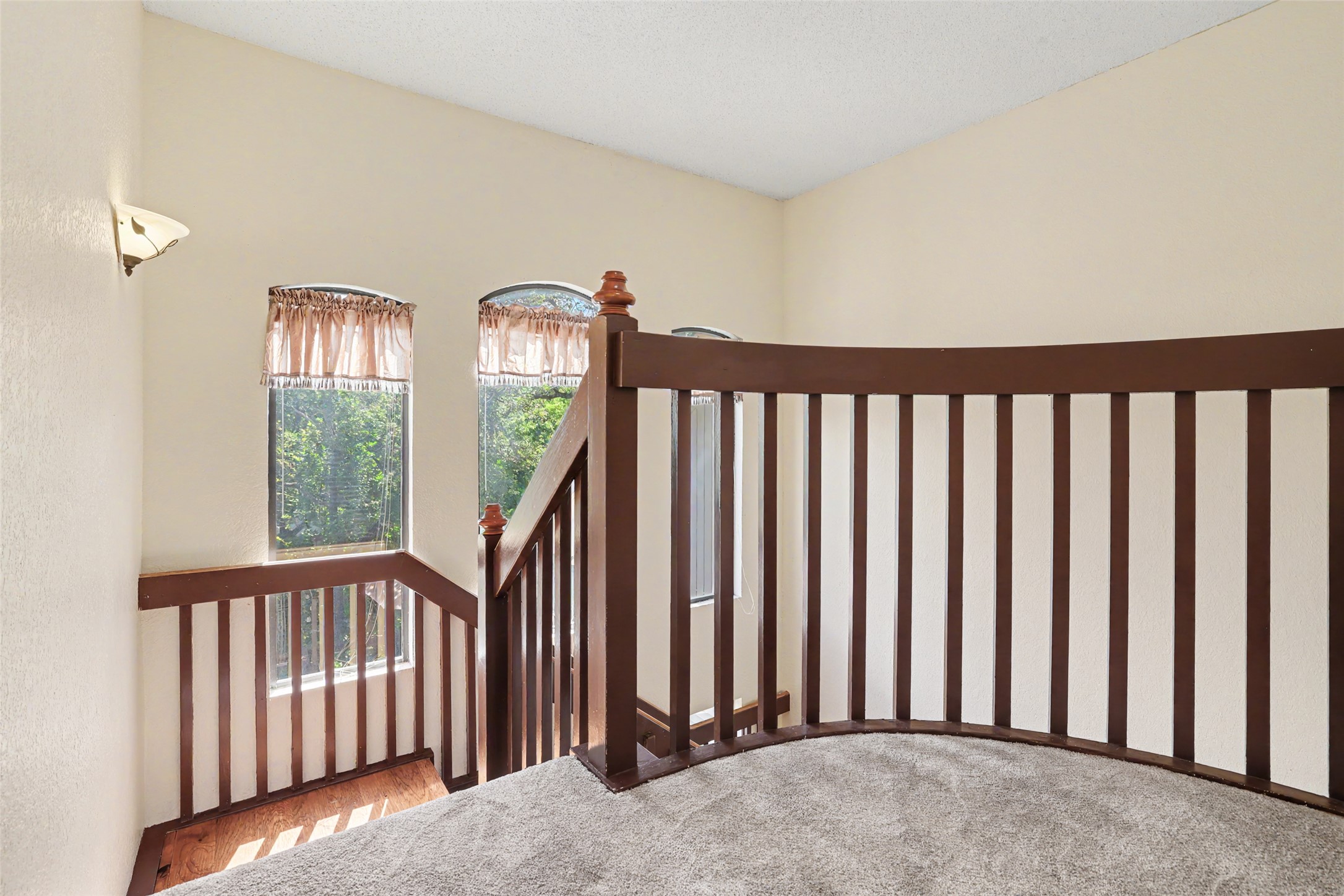 110 South Ridge Circle Georgetown, TX 78628 - Photo 24 of 37 Carpeted landing featuring a curved wood-finish railing, two large arched windows, a sconce wall fixture, and textured walls