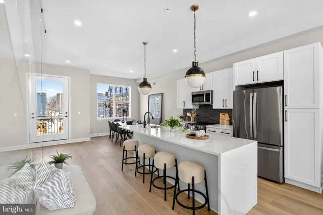 a kitchen with stainless steel appliances granite countertop a refrigerator a stove a sink dishwasher and a dining table with wooden floor