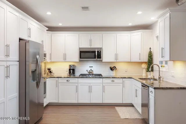 a kitchen with stainless steel appliances granite countertop white cabinets sink and refrigerator