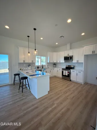 a view of a kitchen with kitchen island a sink wooden floor and stainless steel appliances