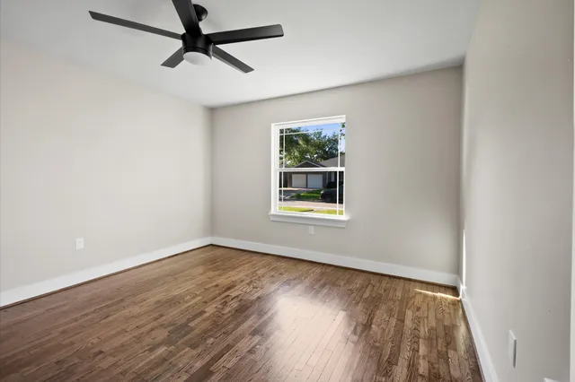 an empty room with wooden floor ceiling fan and windows