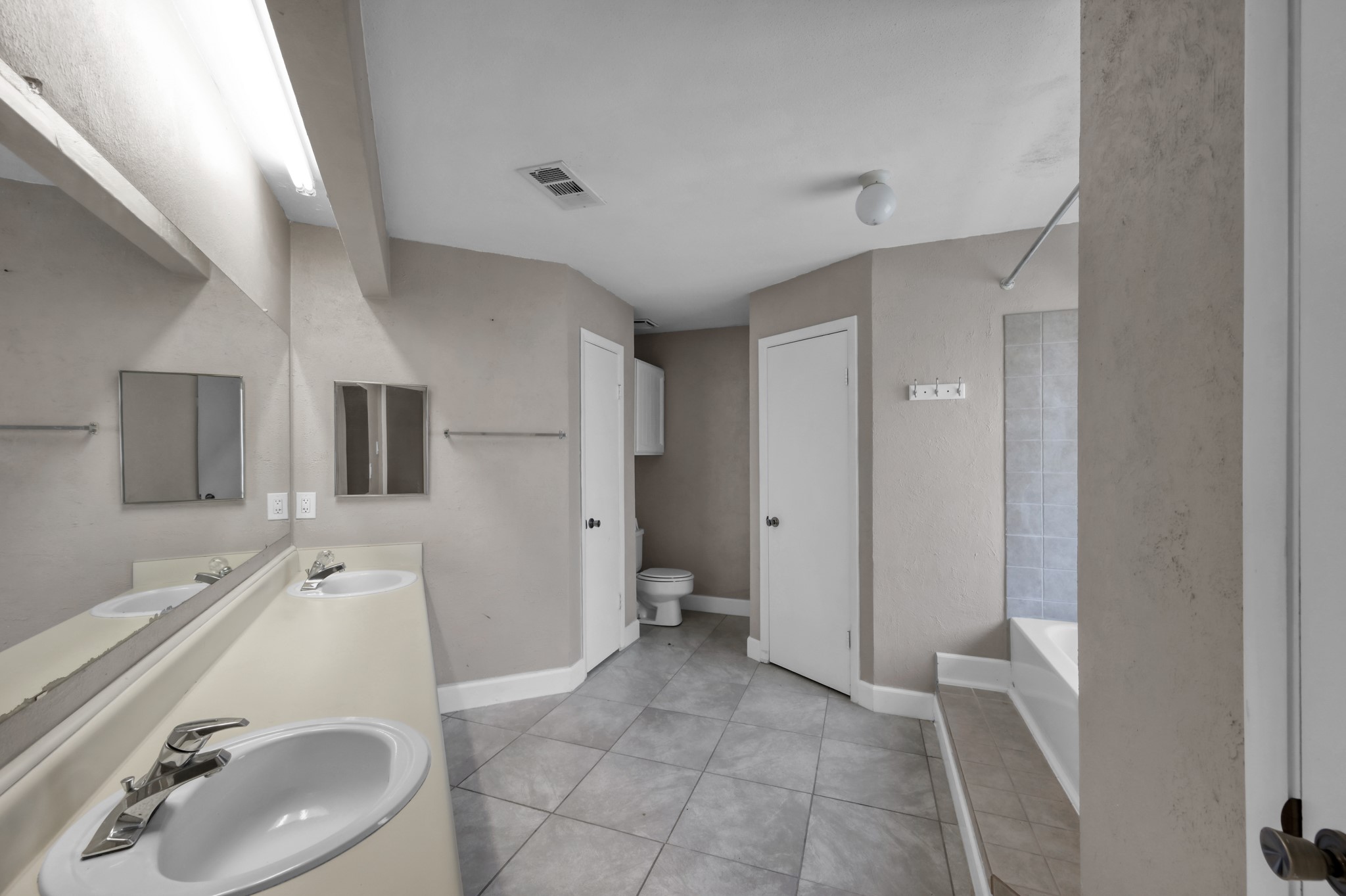 12015 Fallbrook Drive Houston, TX 77065 - Photo 18 of 29 This bathroom features dual sinks with a large mirror, tiled flooring, a bathtub with a shower, and a separate toilet area. The neutral color palette adds a modern touch.