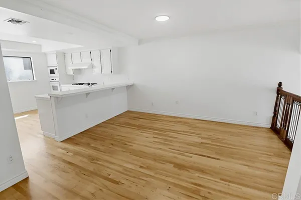 a view of kitchen and empty room with wooden floor