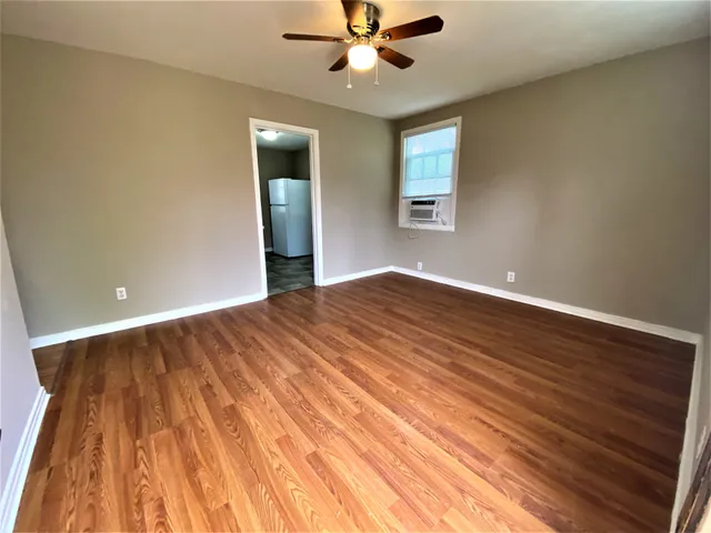 a view of an empty room with wooden floor and a ceiling fan