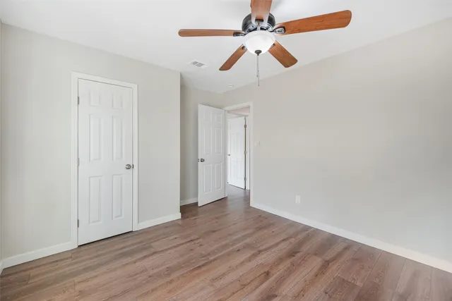 an empty room with wooden floor fan and windows